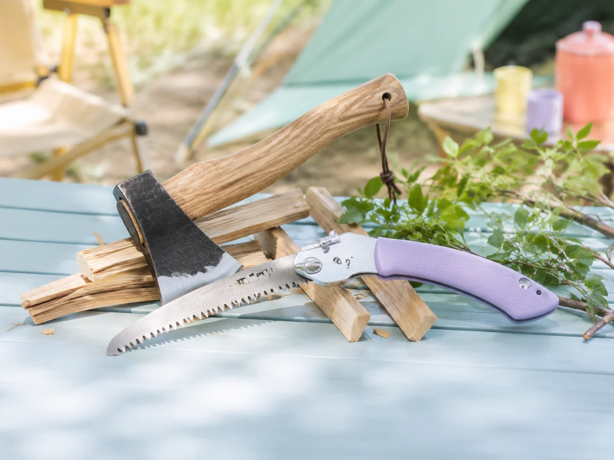A compact camp axe and folding saw arranged with split kindling for cutting and clearing.