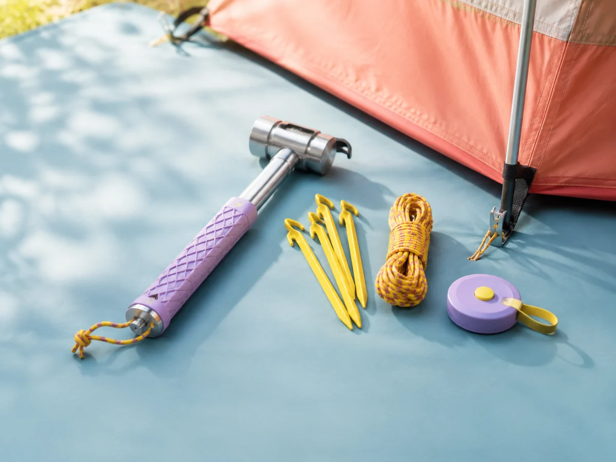 A camping mallet, tent pegs, guyline, and peg puller arranged for shelter setup.